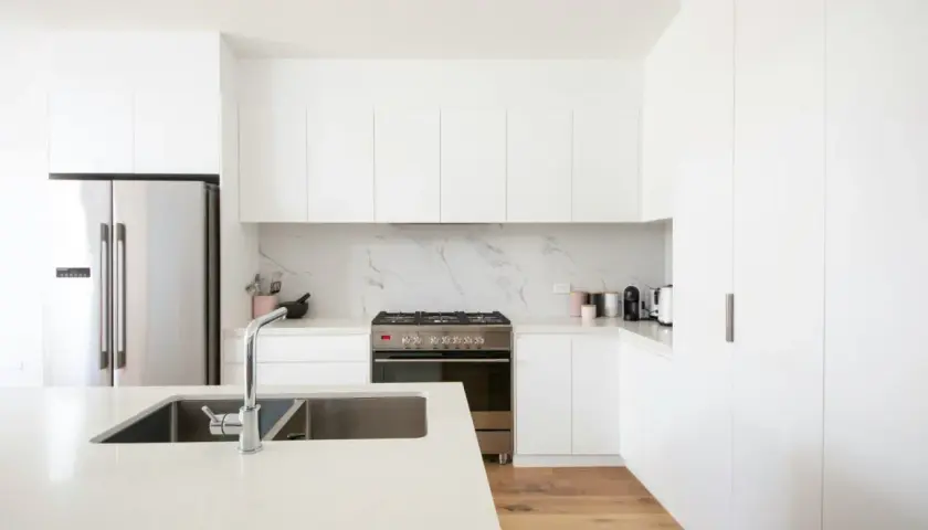 Cocinas modernas blancas con electrodomésticos de acero inoxidable, encimera de cuarzo y suelo de madera.