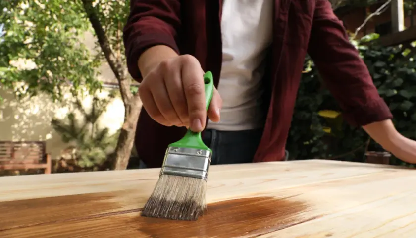 Persona aplica protector a madera con brocha verde. Aprende como impermeabilizar madera para protegerla.
