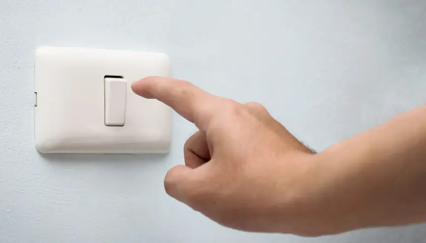 Dedo presionando un conmutador blanco en una pared azul claro.
