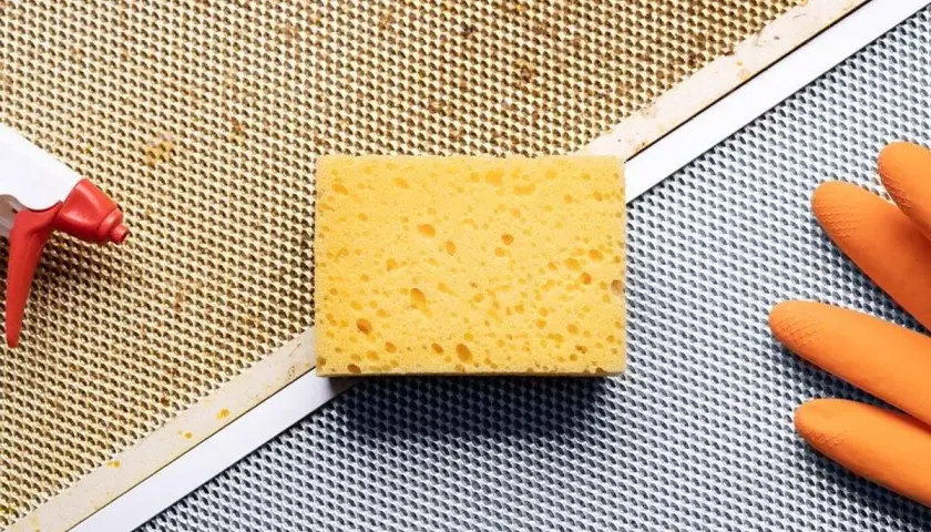 Esponja, guantes naranjas y spray listos para limpiar extractor cocina.