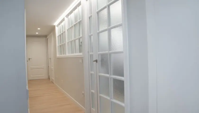 Pasillo con puertas blancas y vidrios emplomados, destacando la variedad de **colores de puertas** en un diseño moderno y luminoso.