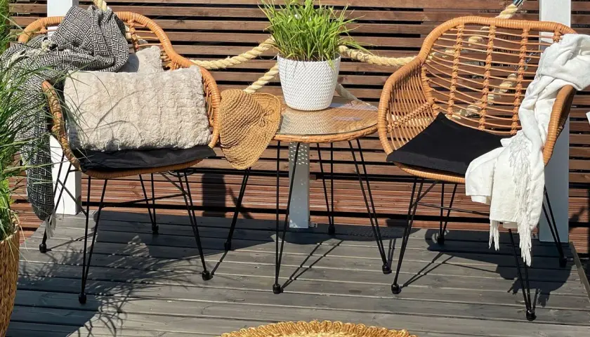 Dos sillas de mimbre con cojines y mantas, una mesa auxiliar con planta y un sombrero de paja. Decoración de mini balcones acogedora.