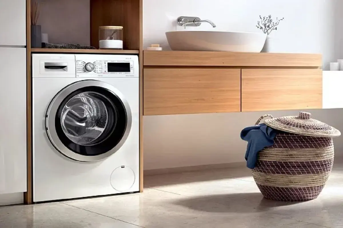 Lavadora moderna lista para instalar en un baño con cesta de ropa sucia.