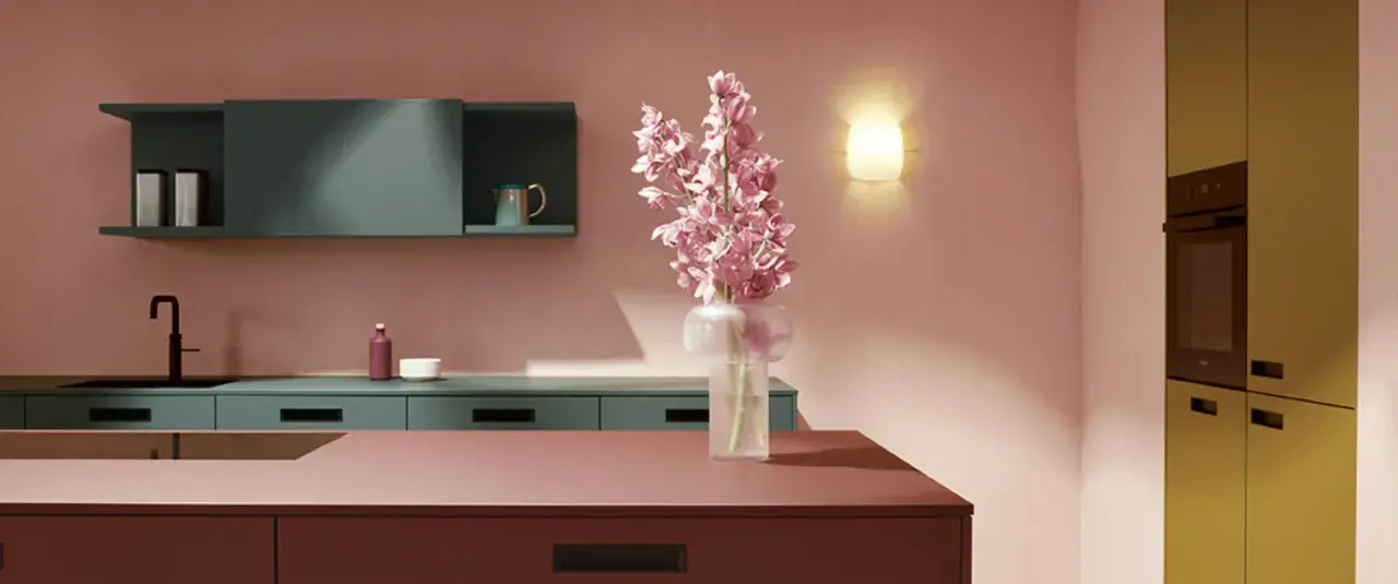 Elegante cocina con una **combinación de colores para cocina** audaz: rosa empolvado, verde azulado y detalles en burdeos y ocre. Flores rosas en un jarrón.