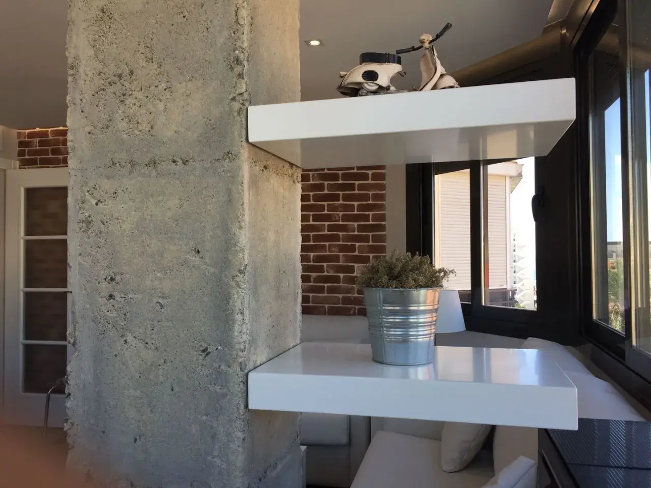 Ideas para decorar columnas dentro de la casa: estantes blancos flotantes con un modelo de Vespa y una planta en lata.