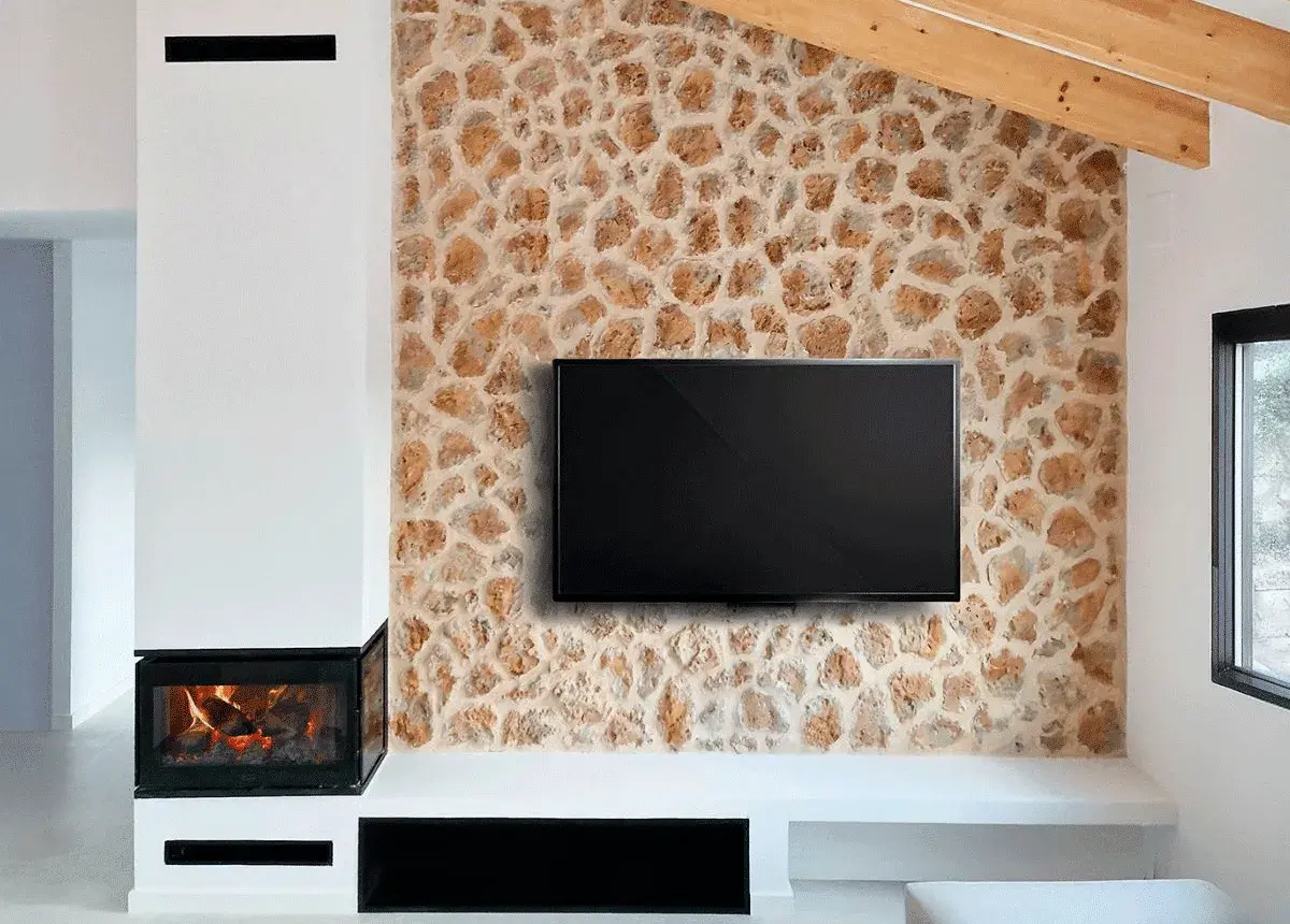 Televisor colgado sobre una pared con un rústico revestimiento de piedra natural, junto a una chimenea moderna.
