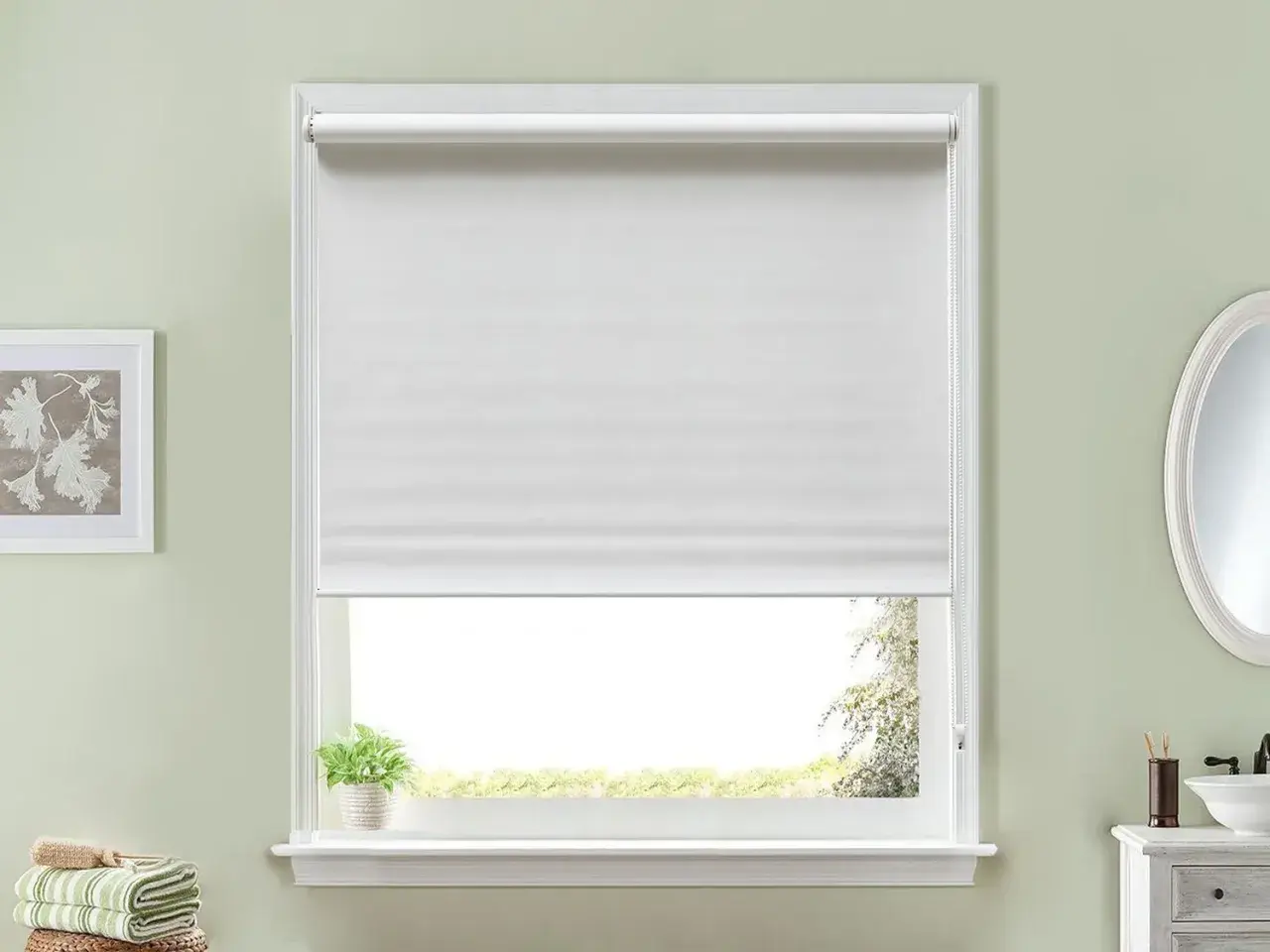 Ventana con estor enrollable blanco, ideal para aprender cómo hacer un estor. Al lado, un cuadro y toallas.