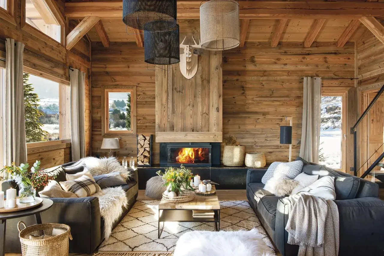 Acogedor salón con chimenea encendida, sofás grises, alfombra de rombos y mucha madera. La decoración casa rústica perfecta para el invierno.