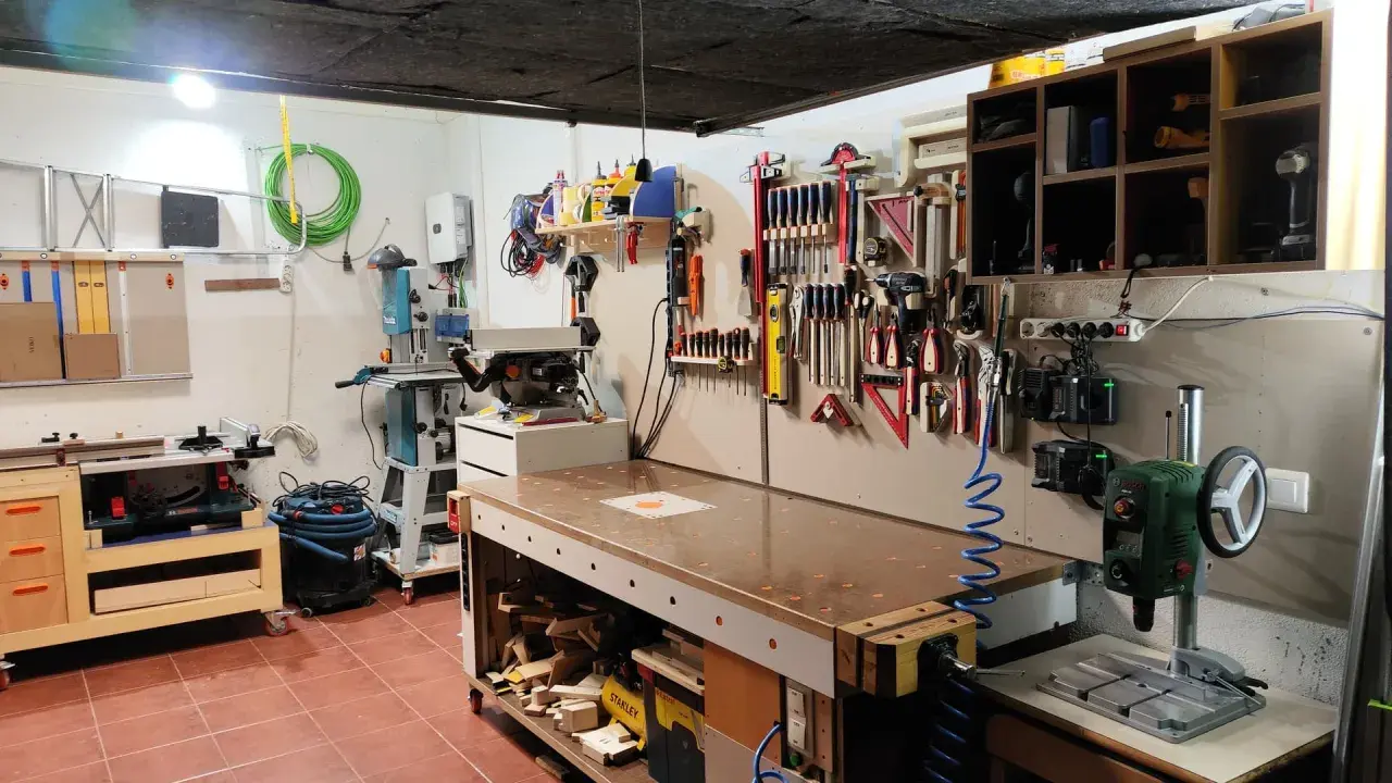 Un completo taller en casa con banco de trabajo, sierra de calar, taladro de columna y herramientas organizadas en la pared.