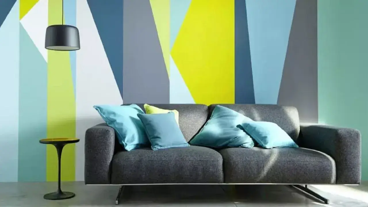 Sofá gris con cojines turques frente a pared con diseño geométrico en colores vivos. ¡Ideas para pintar paredes originales!