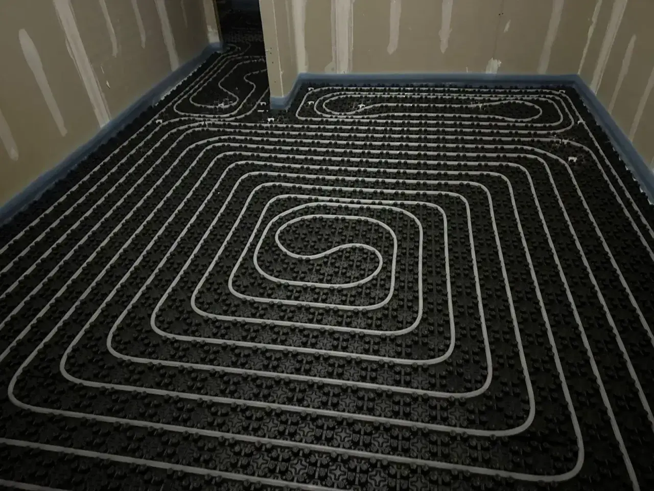 Instalación de tuberías para suelo radiante eléctrico. Se observan las espirales de calefacción sobre una base negra, listas para ser cubiertas.