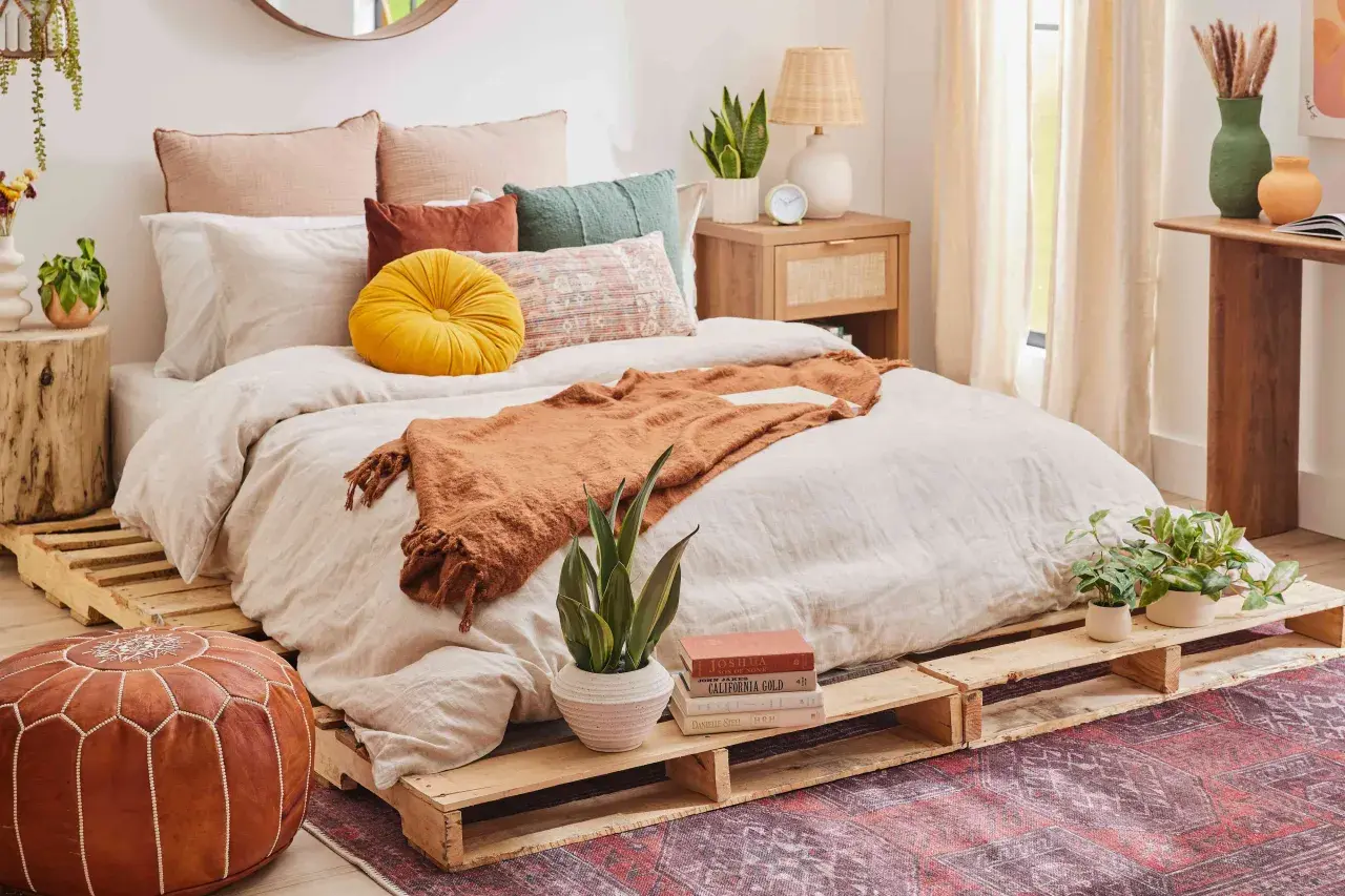 Cama acogedora con cómodas camas hechas con palets, cojines coloridos y manta naranja.
