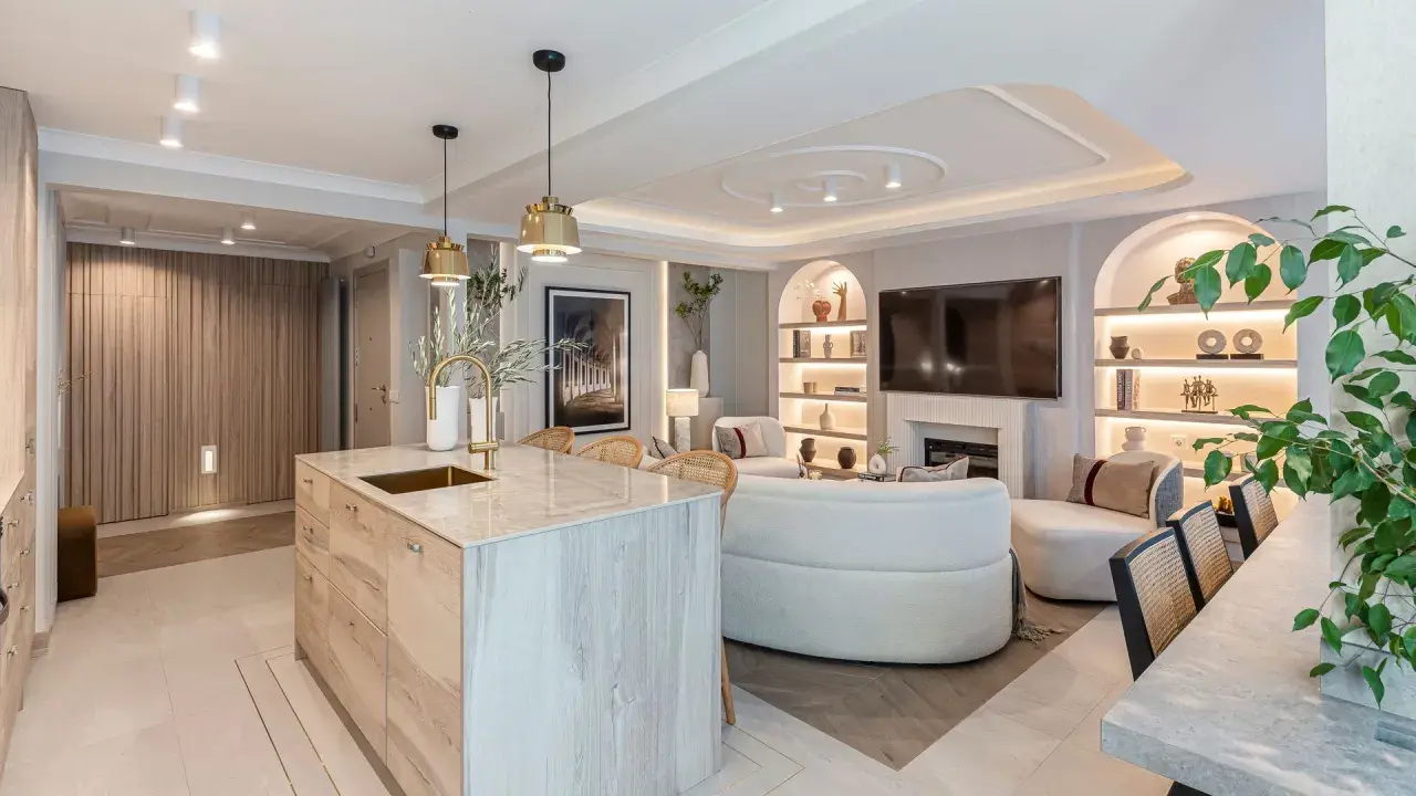 Cocina y sala de estar modernas con isla de mármol, sofás curvos y estanterías iluminadas. La iluminación ambiental crea una atmósfera acogedora, con suficientes **lúmenes por m2** para cada rincón.