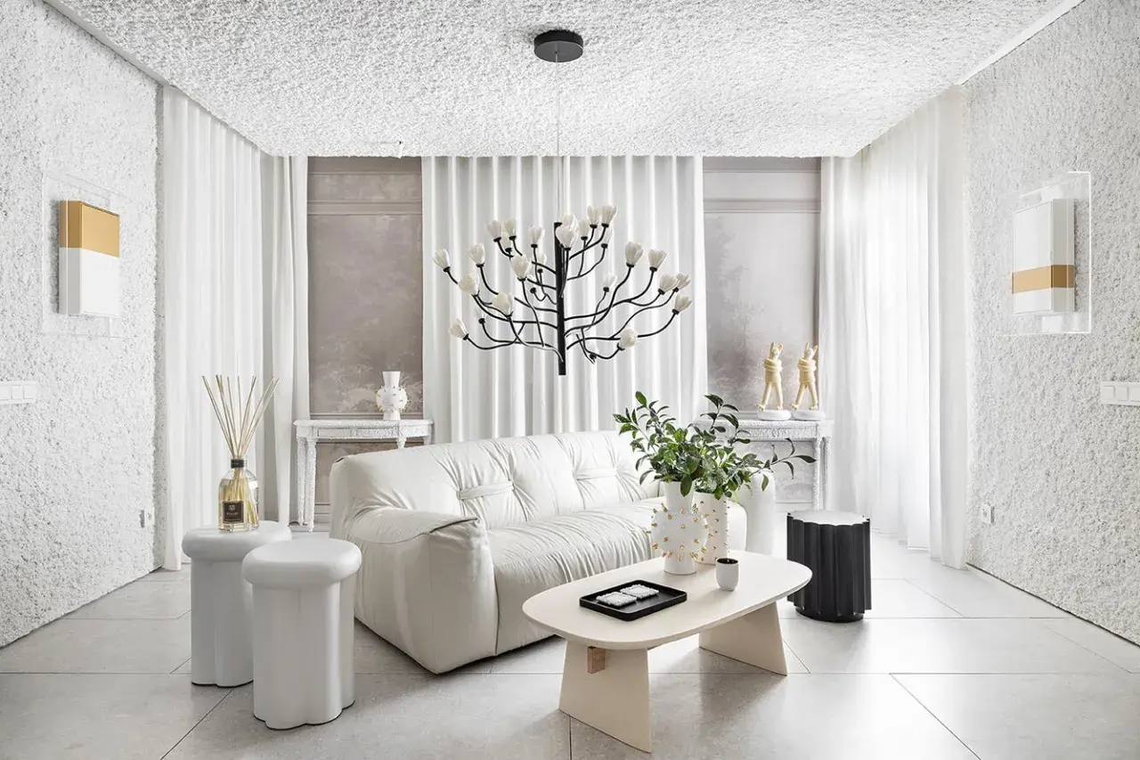 Salón minimalista con sofá blanco, mesa de centro ovalada y **gotele moderno** en paredes y techo. Lámpara escultural y cortinas blancas completan el espacio.