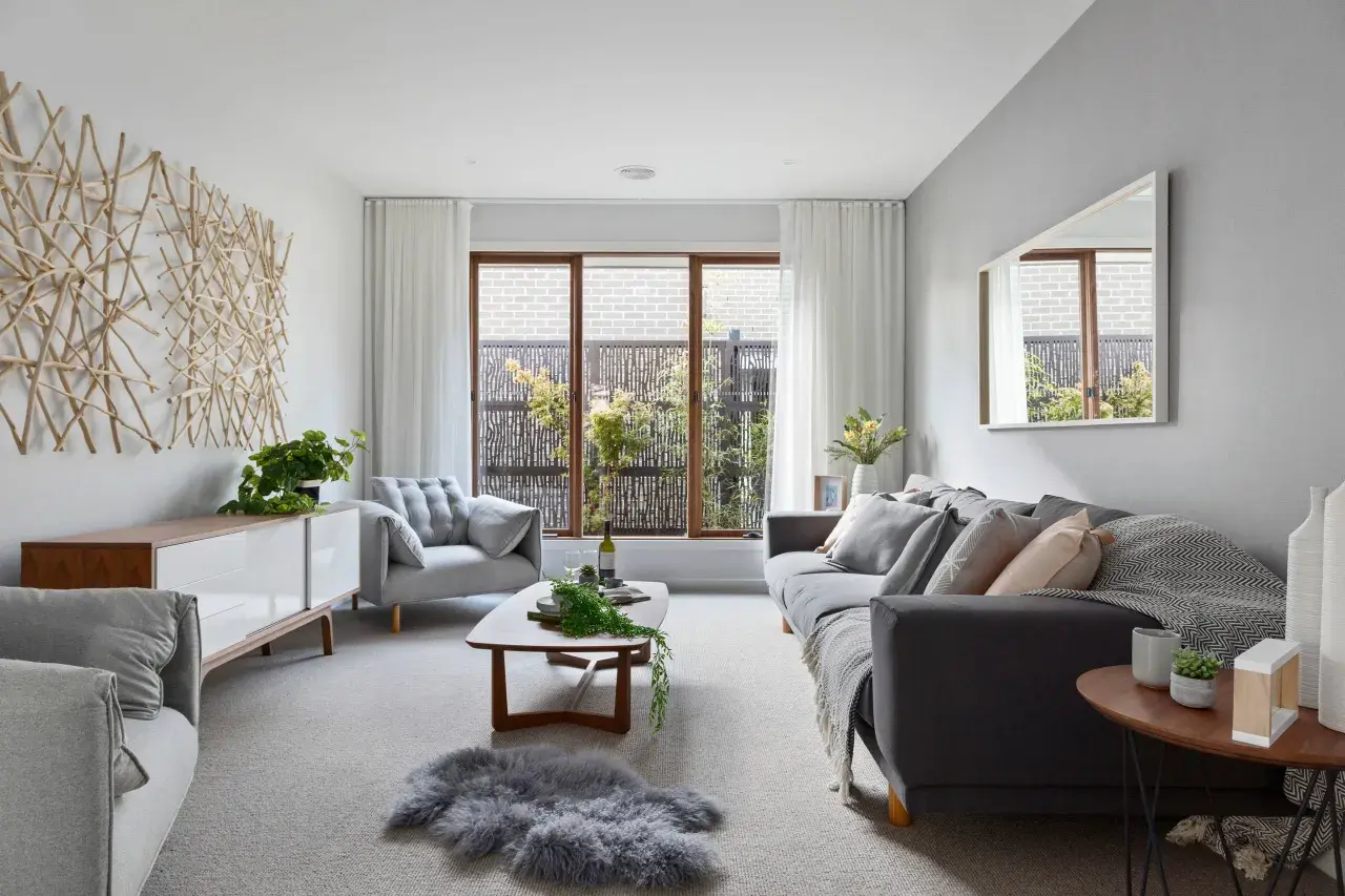 Salón moderno con sofás grises, mesa de centro de madera y arte de pared de ramas. Las paredes color gris crean un ambiente sereno.
