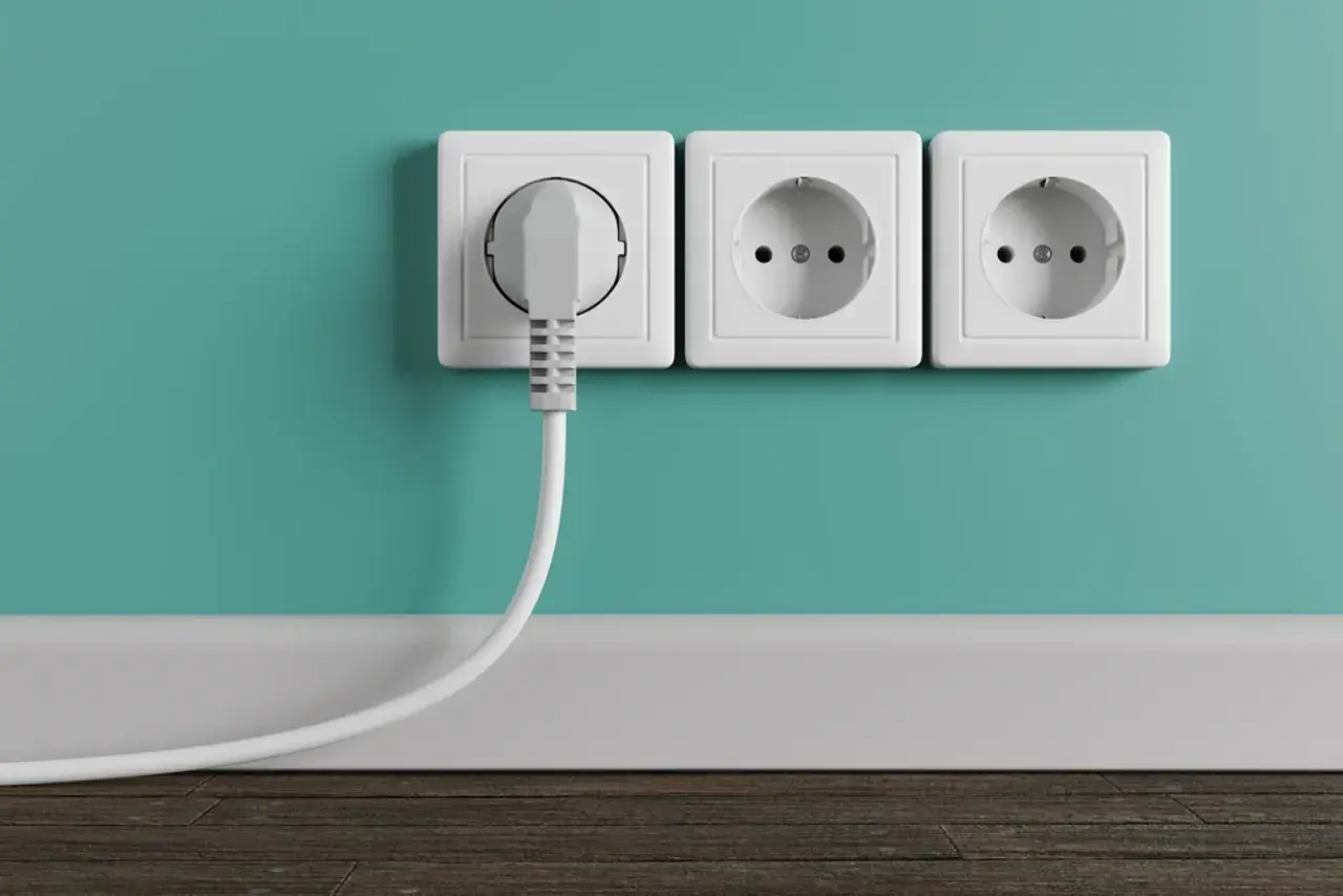 Tres enchufes blancos en una pared turquesa. Uno tiene un enchufe gris conectado. La altura de los enchufes en la cocina es estándar.