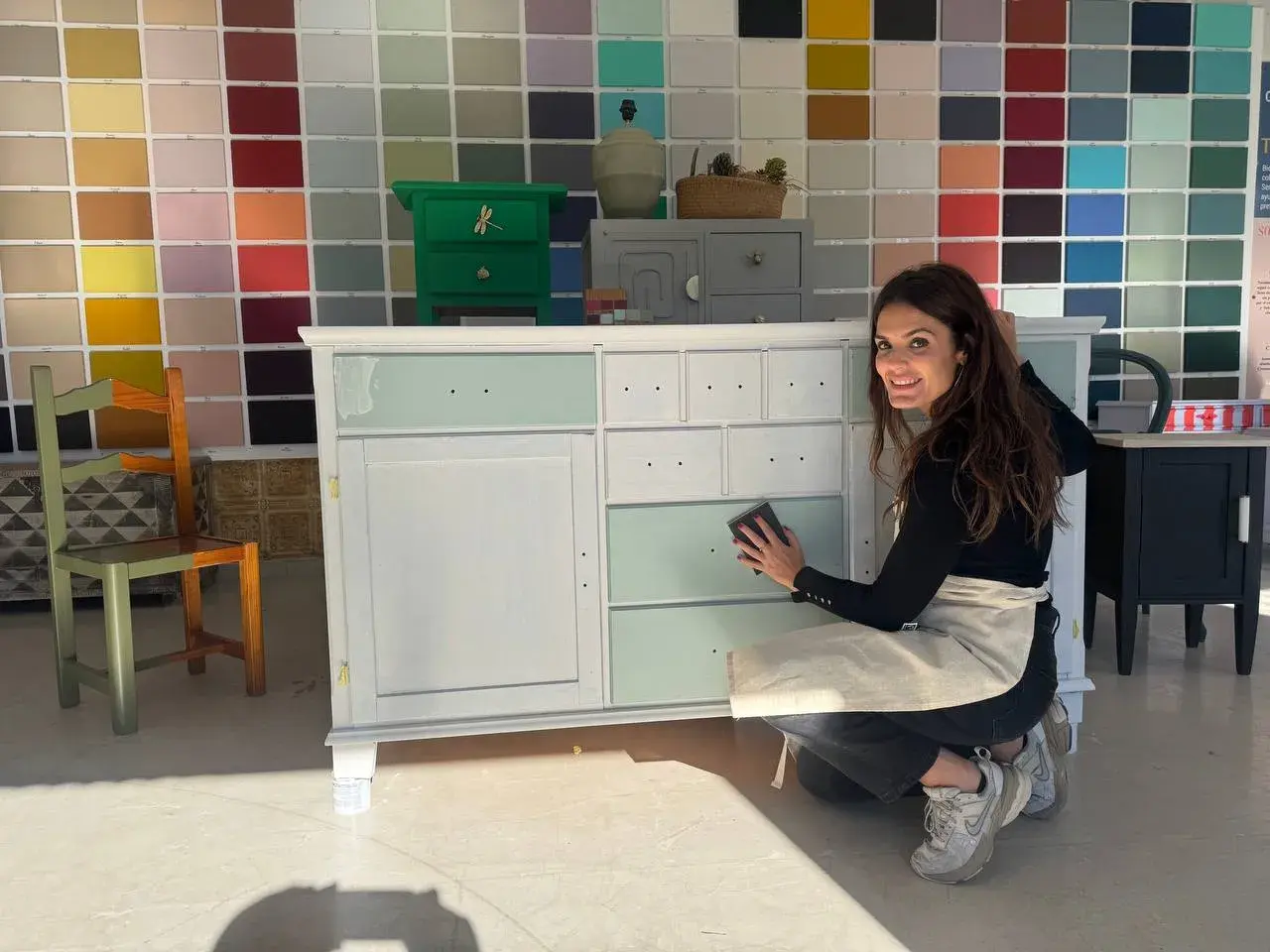 Mujer sonríe mientras lija un mueble de madera, mostrando cómo pintar un mueble de madera con un toque de color.