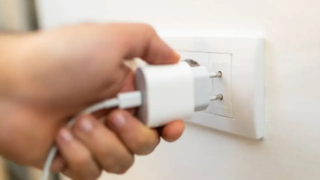 Mano insertando un cargador blanco en un enchufe de pared. Solución fácil de **enchufe sin obra** para cargar dispositivos.