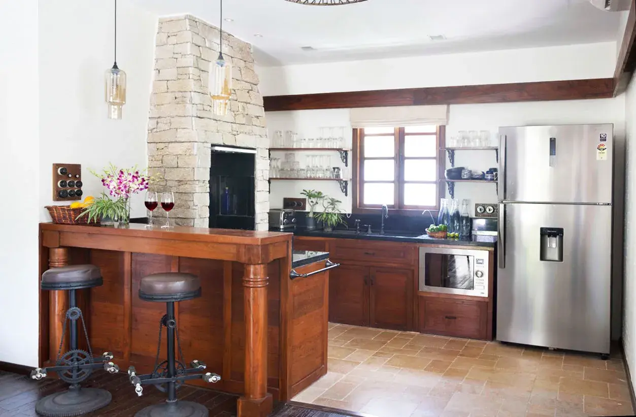 Cocinas con chimenea de piedra, barra de madera con taburetes, electrodomésticos de acero inoxidable y ventana rústica.