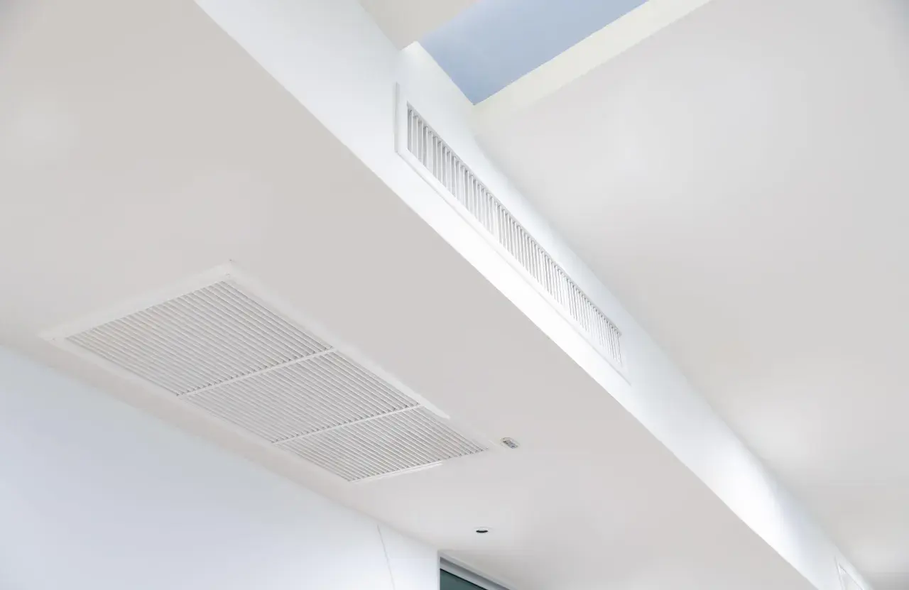 Rejillas de aire acondicionado integradas en un falso techo blanco, con conductos ocultos para una climatización discreta.