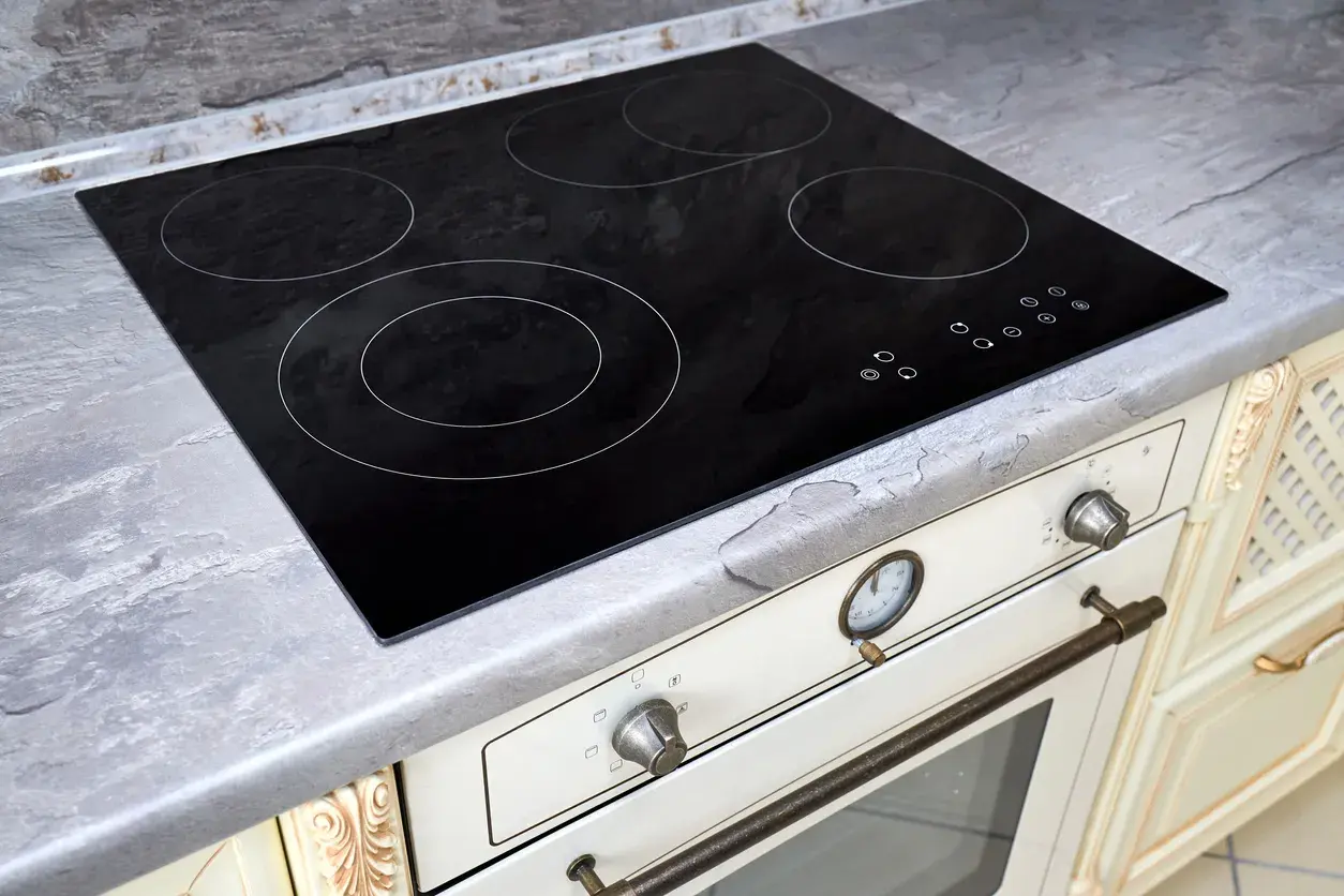 Placa de cocina vitrocerámica negra con cuatro zonas de calor y controles táctiles. Encimera gris piedra.
