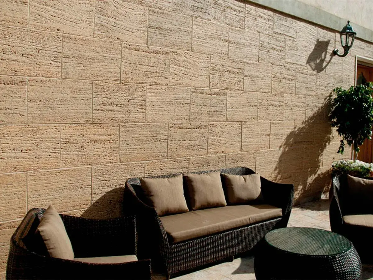 Un patio acogedor con muebles de mimbre y cojines marrones, rodeado de patios con paredes de piedra natural.