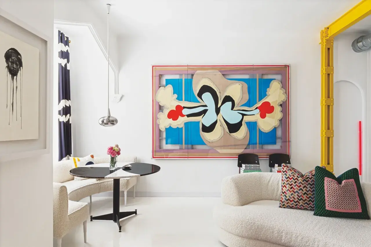 Un salón moderno con arte abstracto y muebles curvos. Sofás blancos texturizados y una mesa redonda negra y blanca crean sencillas salas pequeñas.