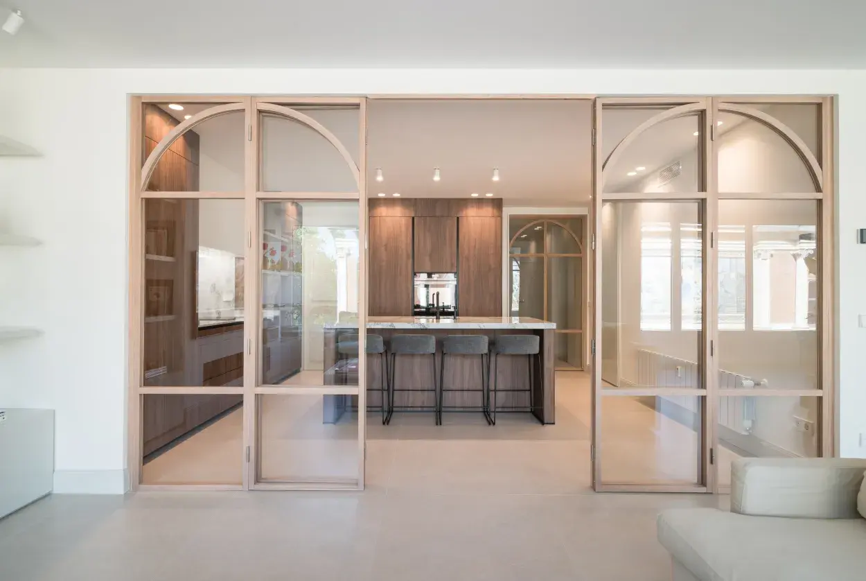Moderna cocina semiabierta cristal con isla central y taburetes. Muebles de madera oscura y encimera de mármol.