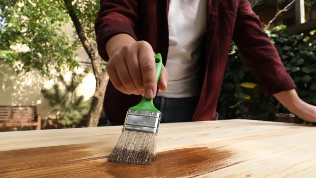 Persona aplica protector a madera con brocha verde. Aprende como impermeabilizar madera para protegerla.
