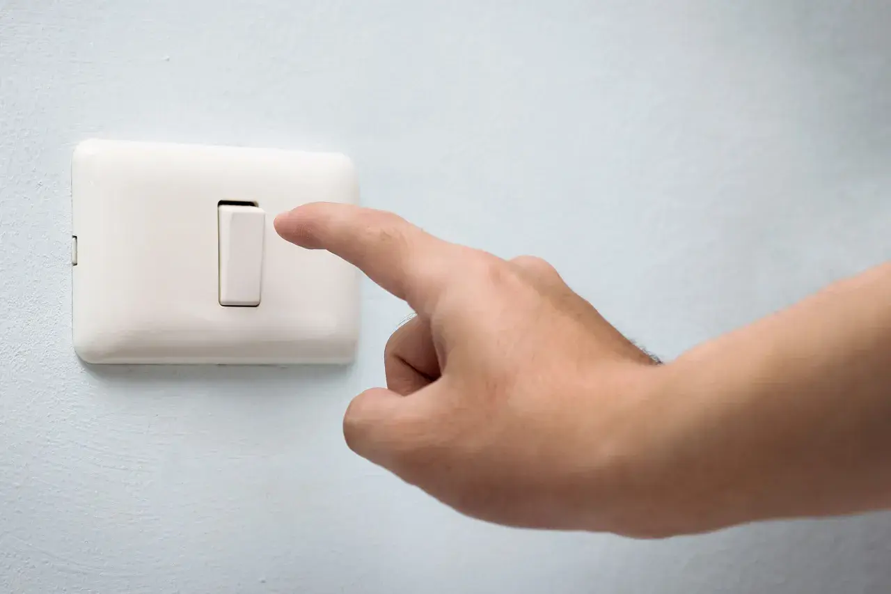 Dedo presionando un conmutador blanco en una pared azul claro.