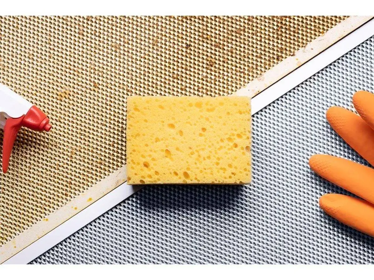Esponja, guantes naranjas y spray listos para limpiar extractor cocina.