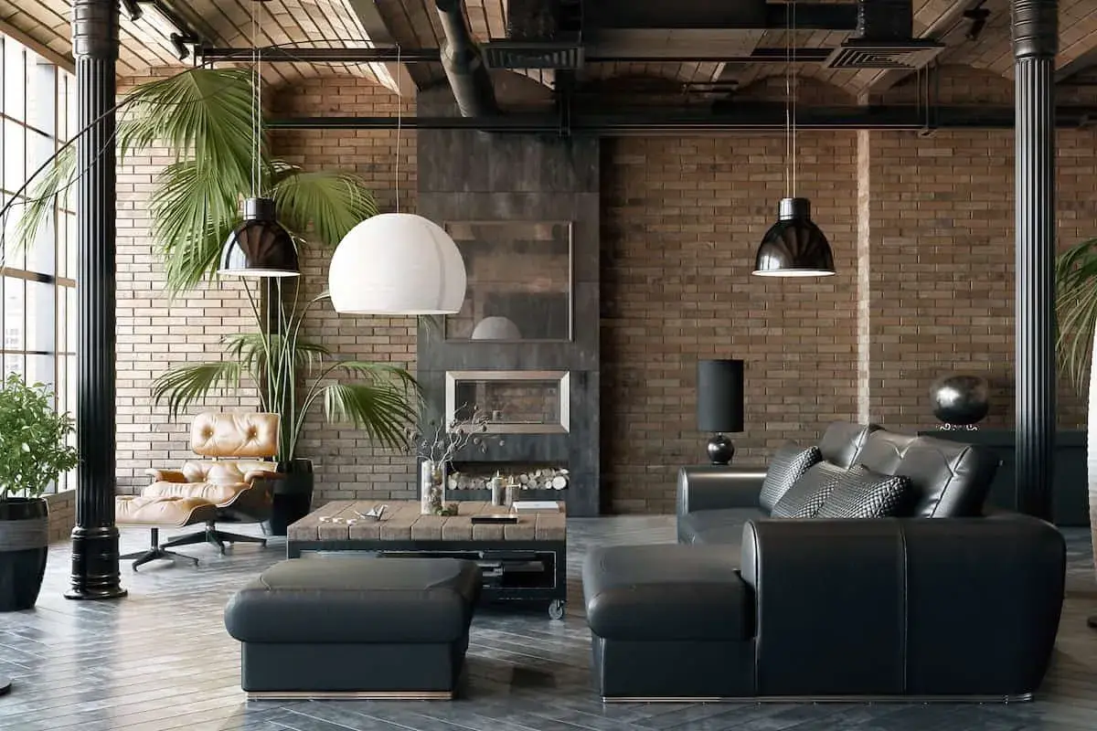 Sofá de cuero negro y sillón de cuero marrón junto a paredes estilo industrial de ladrillo visto. Chimenea y plantas verdes completan el ambiente.