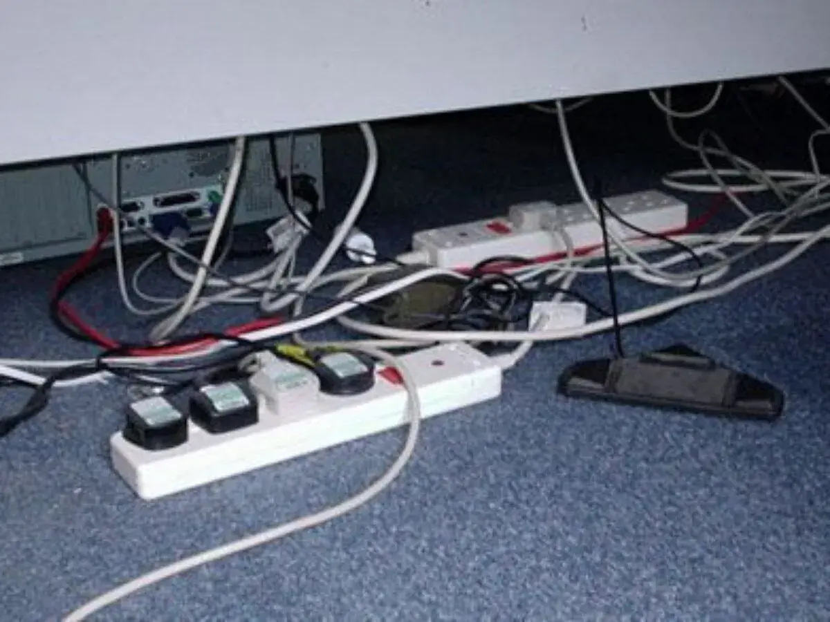 Un enredo de cables y regletas bajo un escritorio. Un ejemplo de qué es un contacto eléctrico indirecto, con cables expuestos y enchufes.
