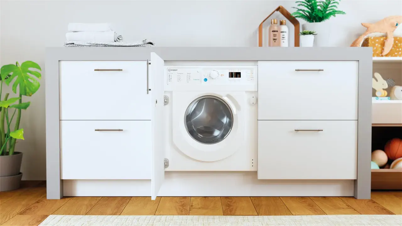 Lavadora Indesit con puerta abierta, lista para el lavado. El desague lavadora está oculto tras el mueble.