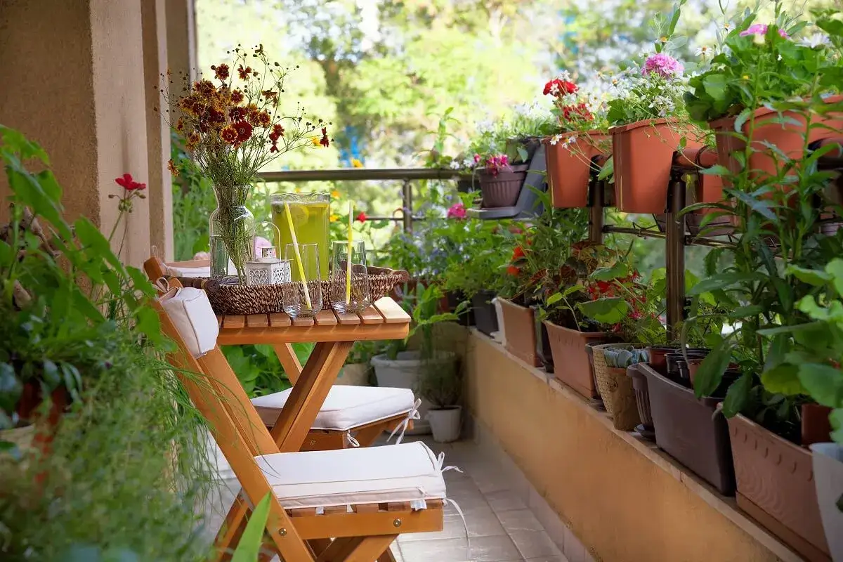 Un balc&oacute;n acogedor con mesa de madera, sillas y muchas plantas. La decoraci&oacute;n de mini balcones crea un oasis verde.