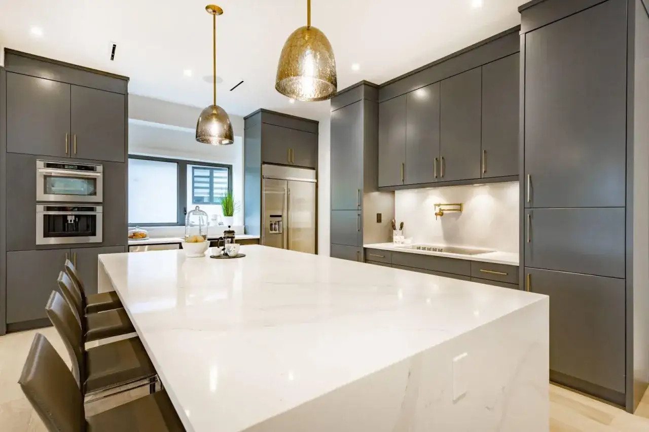Cocina moderna con isla de cuarzo blanco. Dos lámparas colgantes doradas iluminan el espacio, mostrando cómo iluminar una cocina con estilo.