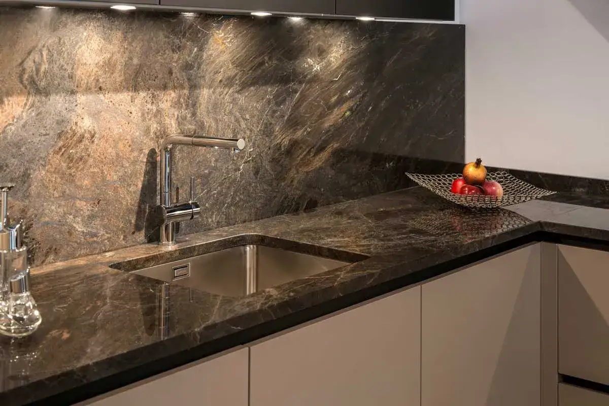 Encimera de cocina con veteado marrón y dorado, mostrando la diferencia entre granito y mármol. Un fregadero de acero inoxidable y un grifo cromado.