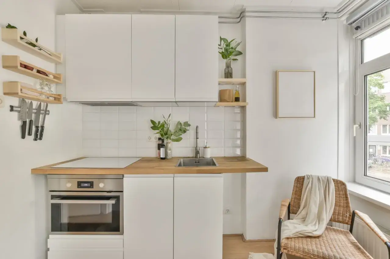 Cocina moderna y funcional, ideal para reformas de cocinas pequeñas. Muebles blancos, encimera de madera y electrodomésticos integrados.