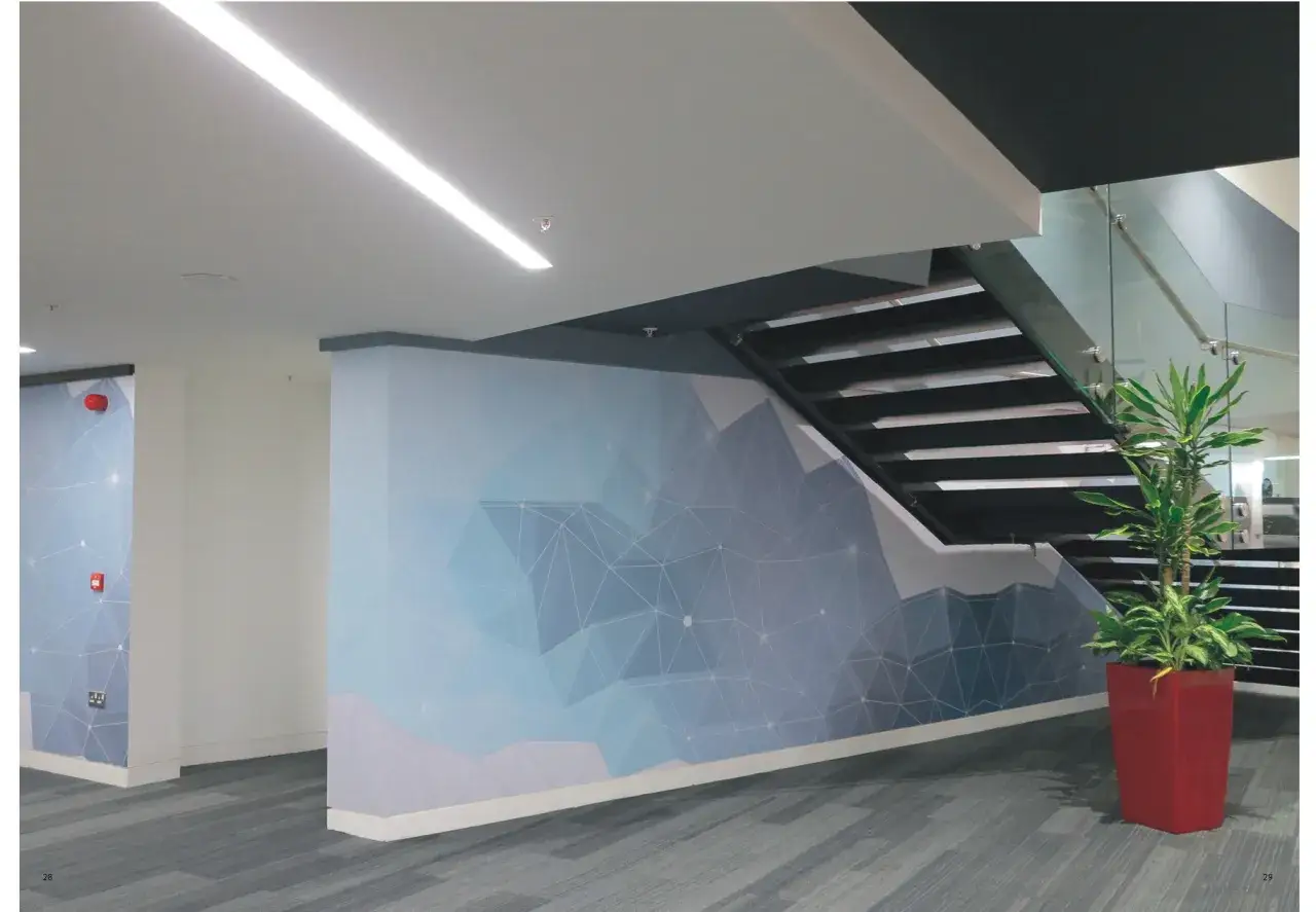 Modern oficina con escaleras y murales de diferentes tipos de vinilos con dise&ntilde;o geom&eacute;trico azul. Planta en maceta roja.
