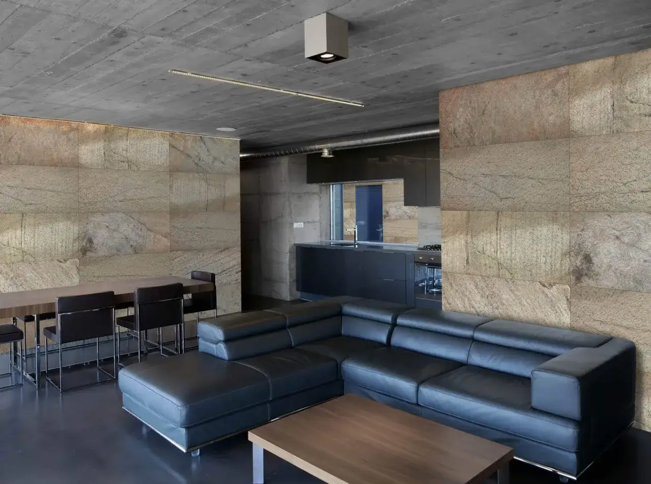 Un salón acogedor con sofá negro, mesa de comedor y paredes de piedra natural.