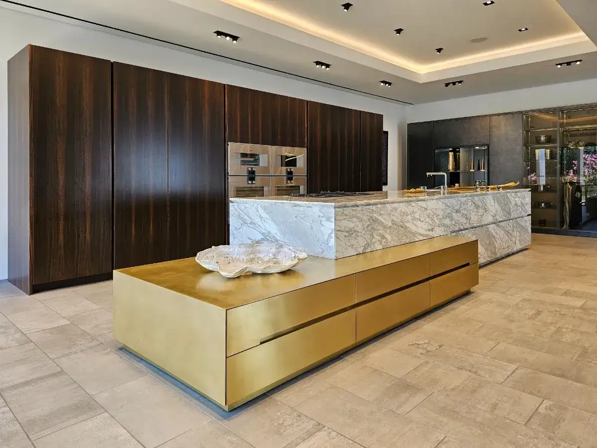 Elegantes diseños de cocinas con gabinetes de madera oscura, isla de mármol y un mueble dorado.