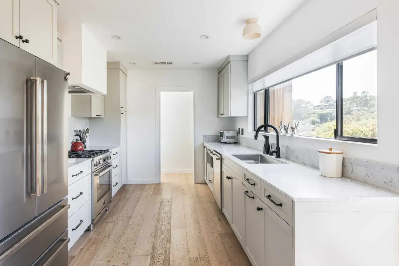 Cocina alargada con electrodom&eacute;sticos de acero inoxidable, encimeras de m&aacute;rmol y gabinetes blancos. Perfecta para distribuir eficientemente el espacio.