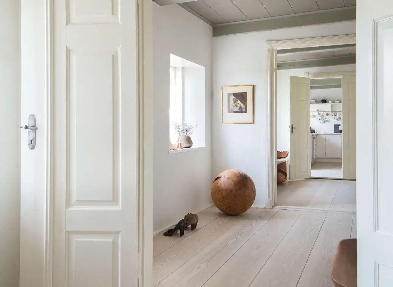 Un pasillo con puertas blancas y suelo de madera clara. Una esfera de madera y unos tacones combinan el suelo y las puertas en este espacio acogedor.
