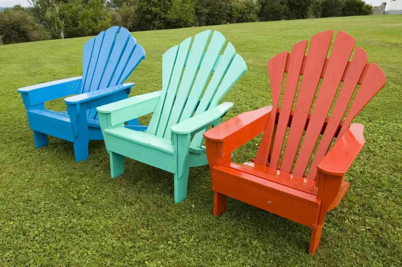 Tres sillas de madera estilo Adirondack, pintadas de azul, verde menta y naranja, lucen vibrantes sobre el césped. ¡Un proyecto de pintar sillas de madera sin lijar que da vida al exterior!