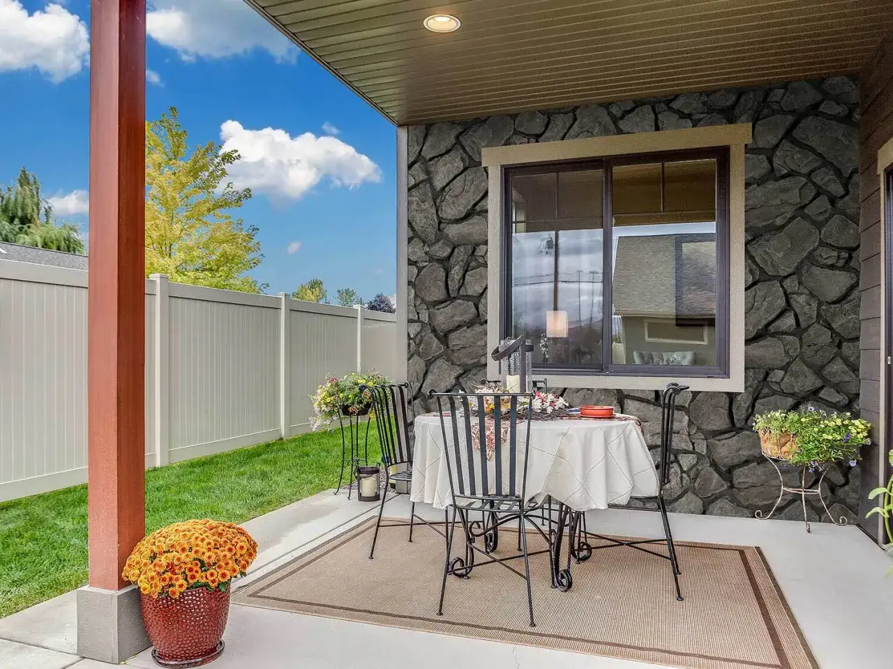 Acogedor patio con mesas y sillas, decorado con flores y un gran jarr&oacute;n de crisantemos. Las patios con paredes de piedra crean un ambiente r&uacute;stico y elegante.
