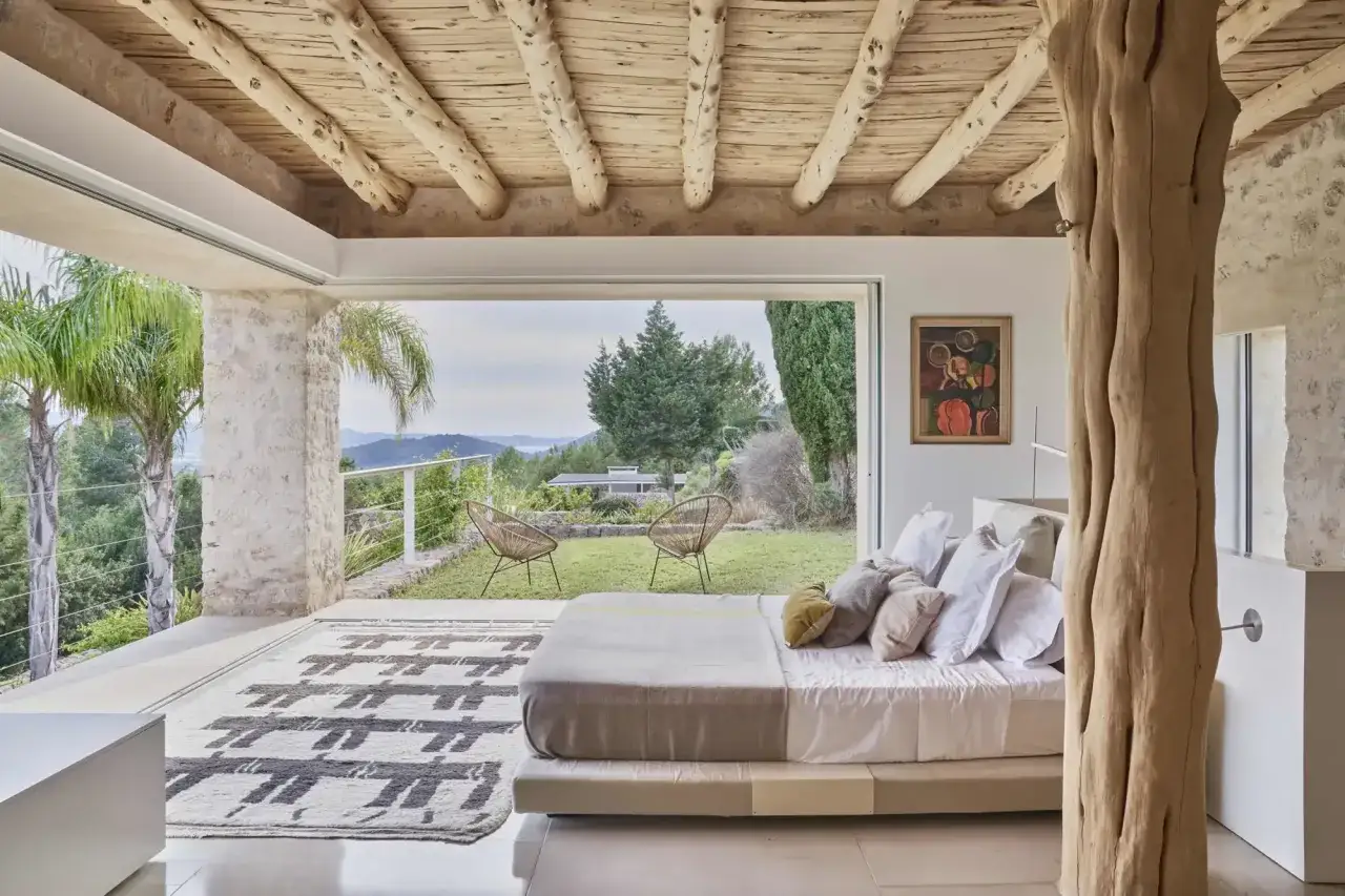 Dormitorio con vistas al mar, techos de madera rústica y elementos naturales que evocan los salones ibicencos.