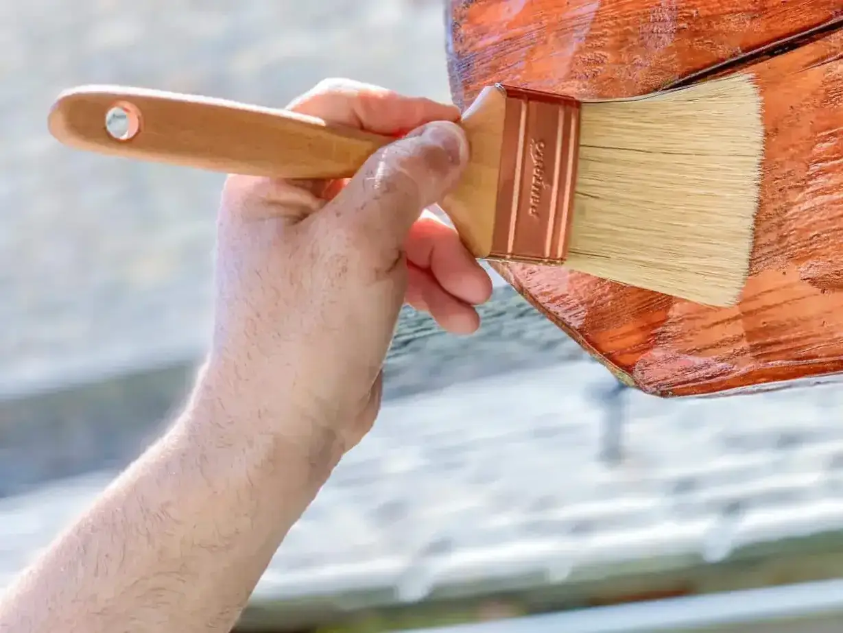 Aplicando el mejor tratamiento para la madera exterior. Una mano con brocha protege la madera, dándole un acabado brillante y duradero.