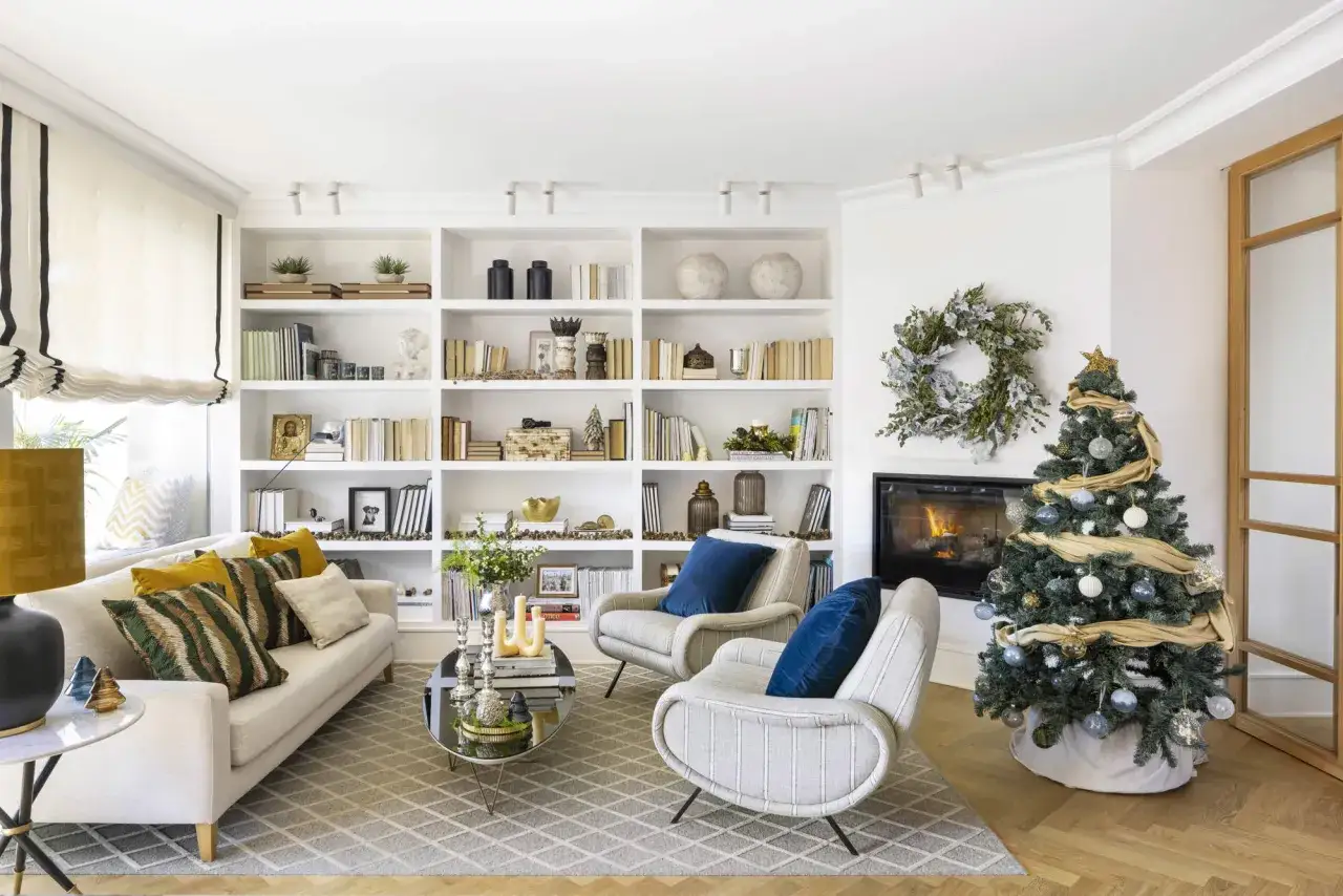 Acogedor sal&oacute;n de navidad con chimenea encendida, &aacute;rbol decorado y estanter&iacute;as llenas de libros y adornos.