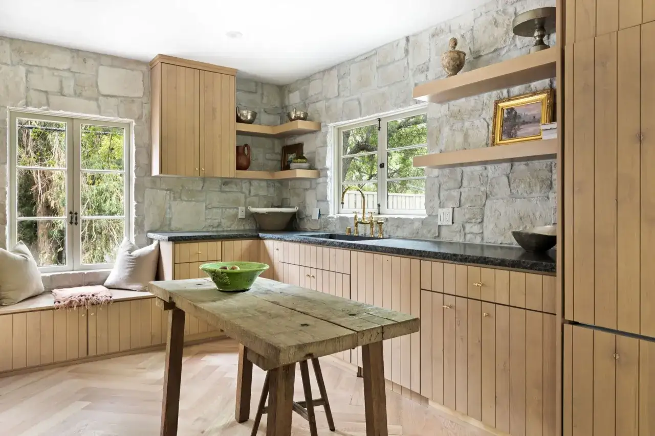 Cocinas con paredes de piedra rústica, gabinetes de madera clara y una mesa de madera desgastada.