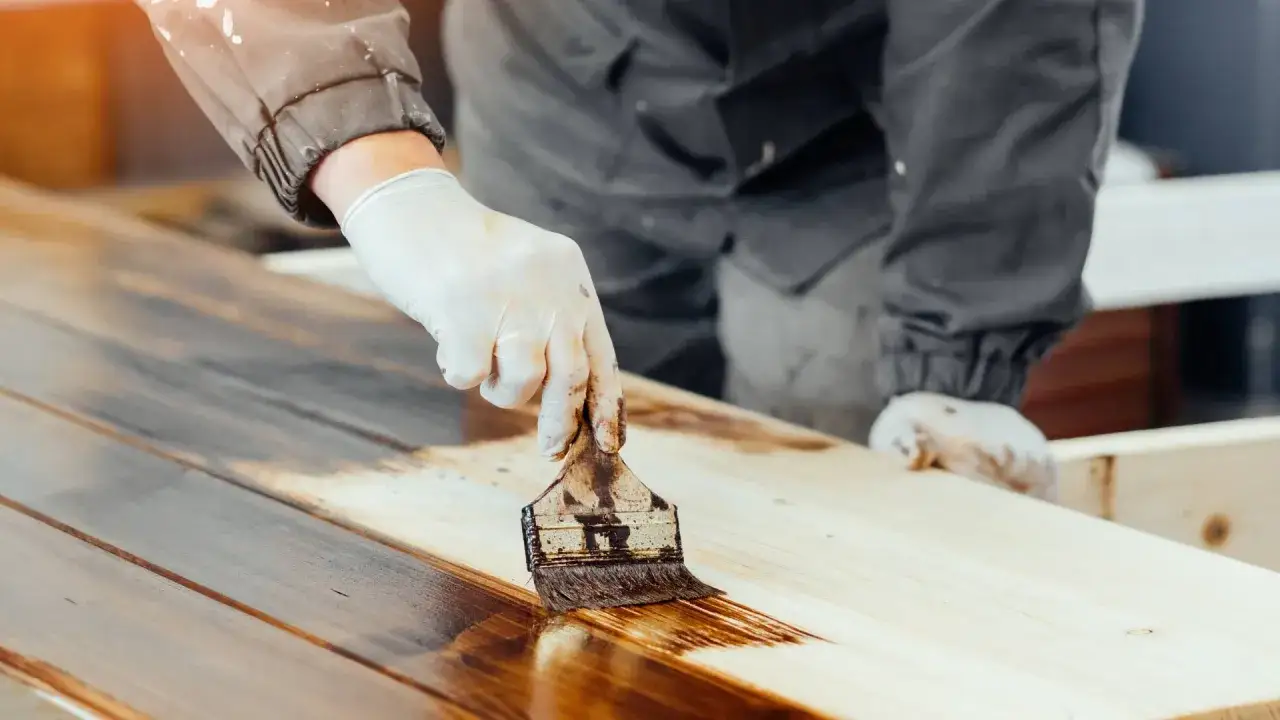 Persona con guantes aplica barniz a una mesa de madera.